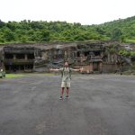 Traveler posing before green hillside rock-carved temple complex