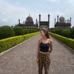 Woman walking toward white-domed Indian temples and green gardens